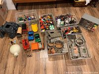 Overall view of plastic totes containing figures, accessories, vehicles, and castle parts arranged on floor