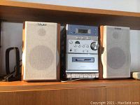 Full micro hi-fi system setup on shelf including central unit, two speakers, and remote control on left side.