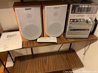 Sony Micro Hi-Fi stereo system setup including main unit, two speakers, remote control, manual, and antennae on wooden shelf.