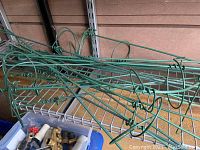 Green metal tomato vine plant stands and trellises with circular and wire mesh shapes, plus a plastic bin of gardening tools including brass and plastic hose fittings.