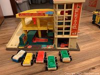 Overall view of Vintage Fisher Price parking garage with elevator, gas pump graphic, ramps, and five vintage cars.