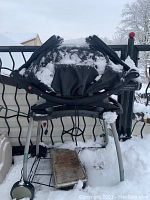 Side and front view of Weber portable BBQ grill with snow on top and grill part folded.
