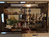 Wide view of all porcelain and ceramic figurines, miniature vase with artificial flowers, teapot, and trinket boxes displayed on shelves.