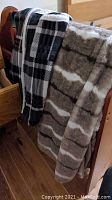 Three blankets draped over a wooden furniture piece showing plaid and patterned designs.