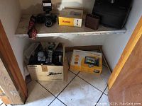 Shelf with Canon AF35M camera, Kodak Easy Share SV811 and C713 cameras in boxes, Zenith VM6200 camcorder box, and Kodak photo frame box