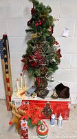 Full lot showing the faux mini Christmas tree in urn with pinecones, red berries, poinsettias, and central metal snowflake ornament; wooden reindeer; American flag pole; window candles; and additional small decorative items on the floor and table in front.