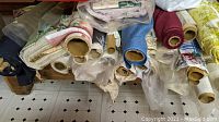 Several rolls of fabric remnants piled, showing different colors and patterns including floral, plaid, and solid fabrics.
