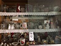 Wide view of cabinet shelves showing assorted figurines, glassware, mugs, collectible teapots.