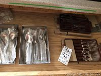 Drawer with multiple sets of flatware forks, spoons, knives wrapped in plastic and some boxed cutlery sets.
