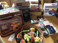 Photo showing entire lot including the Stagecoach model kit box, multiple board games, playing cards, vintage cash register, and colorful wooden spinning tops in a basket.