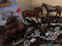 Multiple horse figurines of different sizes and materials grouped together with a box in background