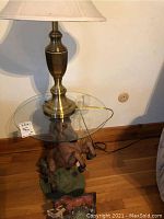 Side view of the horse rearing figure side table with glass top and part of brass lamp visible