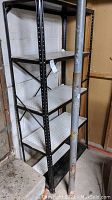 Front and side view of the black metal shelf with four white perforated shelves in a storage area.