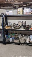 Black metal shelf loaded with pots, pans, kitchenware and boxed appliances.