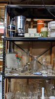 Full view of metal shelves holding kitchen and decorative items including glassware, mugs, and metal containers.
