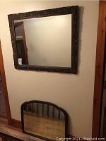 Large rectangular mirror with ornate carved dark wood frame hanging on wall