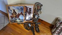 Framed Native American themed paintings resting on floor along with carved wooden and metal decorative wall art pieces