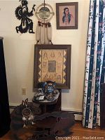 Wide view of wall with three framed Native American wall arts and black metal wolf silhouette art, plus blue ceramic Indian Chief bust and several smaller figurines on table below.
