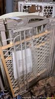 Photo of beige and white pet gates including an Evenflo gate with metal mesh panels, latch mechanism visible, and plastic packaging around parts.