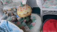 Photo of cactus shaped lamp with desert landscape glass shade, vintage rotary phone with bird figurines, southwestern styled vase, all placed on a glass table with wicker chairs and patterned cushions.