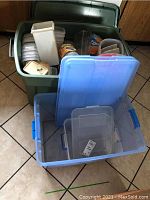 View of large green plastic storage bin filled with smaller plastic containers and some loose lids