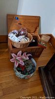 Overall view of the lot showing the wooden box with open lid, woven basket with shells on top, and ceramic pot with artificial flowers on floor.
