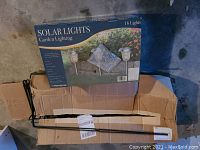 Box labeled Westinghouse Solar Lights Garden Lighting, with 16 lights indicated, placed on a cardboard base along with four metal rods, likely parts of the tool organizer or brackets.