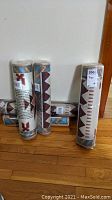Six rolled Southwest printed rugs standing on a hardwood floor leaning against a white wall, showing geometric patterns and tags.