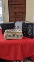 Front view of all storage items on red surface showing black jewelry box, metal box, vintage sewing basket, dark brown box and Tupperware unit