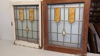 Both stained glass window panels side by side, one in white painted frame and one in natural wood frame