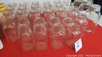31 clear Mason jars of various sizes shown arranged on table, some with lids, mostly clear glass, three jars with embossed D markings visible
