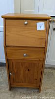 Full front view of closed pine secretary desk showing three sections: top drop-down front panel with knob, a drawer below it, and a lower cabinet door with knob.