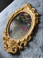 Photo showing the oval mirror laying flat to display floral etched mirror surface and ornate yellow frame design.