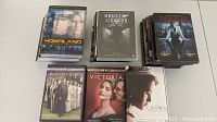 Photo showing six DVD box sets: Homeland (6 seasons), House of Cards (6 seasons), Damages (5 seasons), Downton Abbey (2 seasons), Victoria (season 2), and The Crown (2 seasons) arranged on a flat surface.