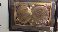 Full view of the framed double globe print showing the two hemispheres and the dark wood frame with gold trim.