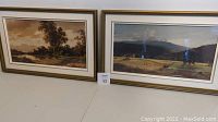 Both framed pastoral scene prints displayed side by side on a table.