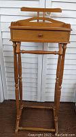 Front view of wooden valet stand showing overall structure including legs, drawer, and clothes hanger.