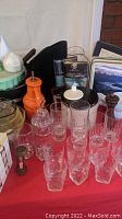 Image shows collection of glassware, ceramic containers, pepper grinder, and packaged cloth napkins or placemats.