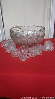 Front angle showing large pressed glass punch bowl surrounded by 15 matching cups on table with red cloth