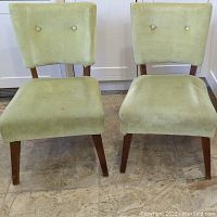 Front view of pair of vintage side chairs with celery green fabric upholstery, showing button back detail and angular wooden legs.
