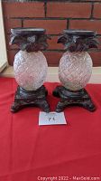 Front view of two matching pineapple candle holders with textured glass and metal claw-footed bases.