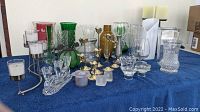 Overview of various glass and crystal vases and candle holders in multiple colors and shapes, arranged on a blue cloth