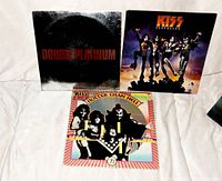 Photo shows four Kiss rock LP vinyl records with worn jackets. Visible are 'Double Platinum,' 'Destroyer,' 'Hotter Than Hell,' and a fourth LP partially visible beneath.