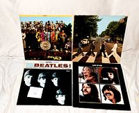 Four Beatles vinyl album covers laid out flat on a white surface showing Sgt. Pepper's Lonely Hearts Club Band, Abbey Road, Meet The Beatles!, and Let It Be.