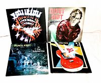 Photo of four assorted rock LP vinyl records upright and spread out: Budgie, Quiet Riot, Mungo Jerry, Electric Angels with visible wear on jackets.