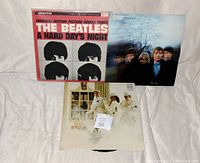 Photo of 3 assorted rock LP albums: The Beatles A Hard Day's Night soundtrack, another Beatles album, and a third LP with a white cover featuring people.