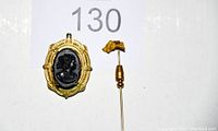Photo showing the black cameo locket with gold-tone ornate frame alongside the gold-tone horse head hat pin.