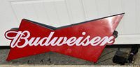 Red and white Budweiser arrow-shaped sign with script logo, approximately 26 inches across, shown against white siding.