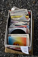 Box of 45 RPM vinyl records stacked vertically, showing a variety of sleeve types and some visible record labels.