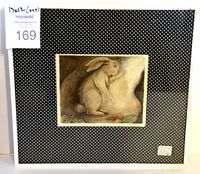 Front view of the framed colored etching featuring a rabbit and a rabbit hole with carrots, mounted on black polka dot background.